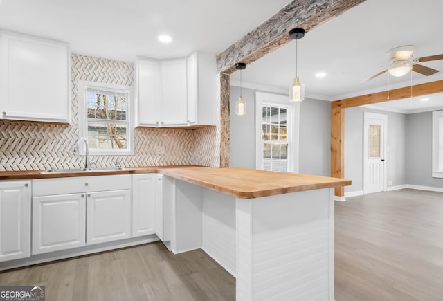 kitchen featuring butcher block countertops, sink, hanging light fixtures, backsplash, and white cabinets