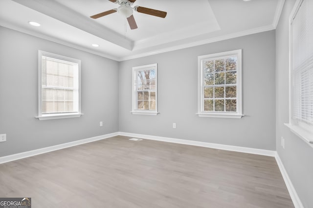 empty room featuring crown molding, a healthy amount of sunlight, a raised ceiling, and light wood-type flooring