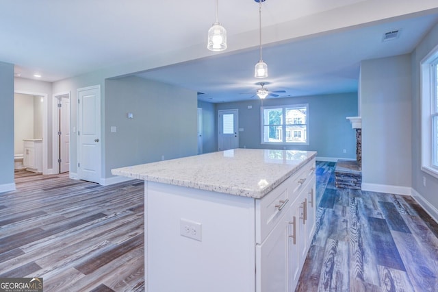 kitchen featuring a stone fireplace, white cabinetry, dark hardwood / wood-style floors, a center island, and decorative light fixtures