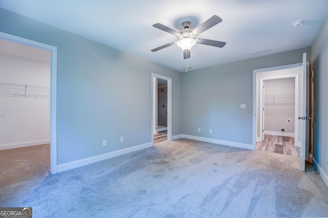 unfurnished bedroom featuring a walk in closet, light colored carpet, ceiling fan, and a closet