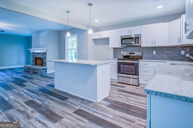 kitchen with sink, stainless steel appliances, light stone countertops, white cabinets, and decorative light fixtures