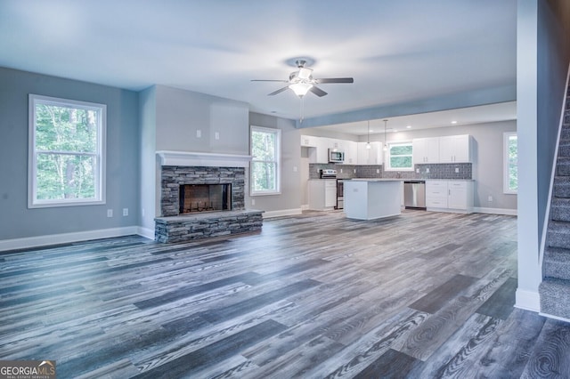 unfurnished living room featuring hardwood / wood-style flooring, a stone fireplace, and ceiling fan