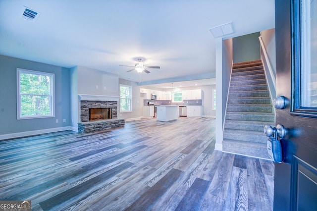 unfurnished living room featuring ceiling fan, a stone fireplace, and hardwood / wood-style floors