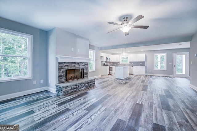 unfurnished living room featuring a stone fireplace, hardwood / wood-style floors, and a wealth of natural light