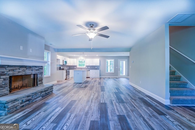 unfurnished living room featuring dark hardwood / wood-style floors, ceiling fan, and a stone fireplace