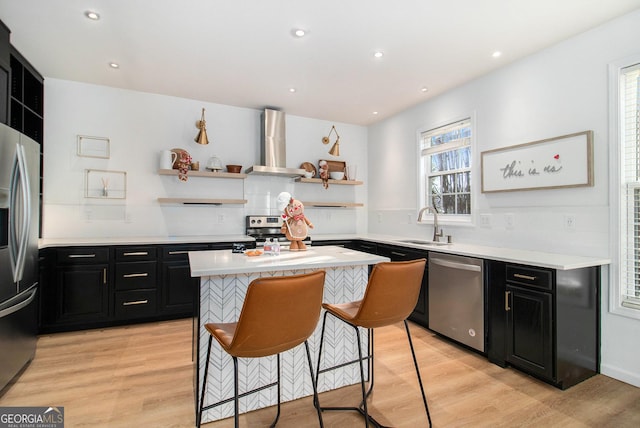 kitchen with a breakfast bar area, light wood-type flooring, a kitchen island, stainless steel appliances, and wall chimney range hood