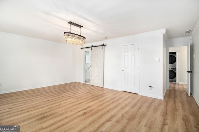 unfurnished bedroom with light hardwood / wood-style flooring, ornamental molding, a barn door, and stacked washer / dryer