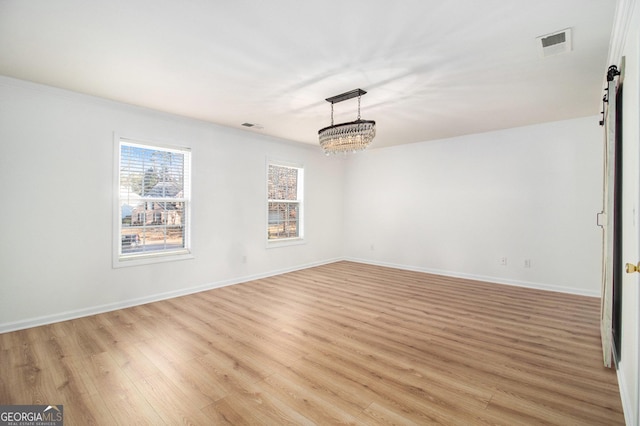 unfurnished room featuring an inviting chandelier, a barn door, and light hardwood / wood-style floors