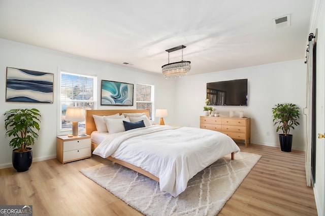 bedroom featuring a barn door, a notable chandelier, and light hardwood / wood-style flooring