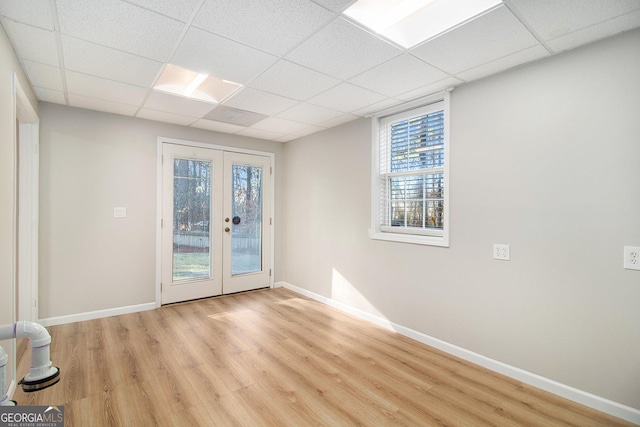 empty room with a drop ceiling, light wood-type flooring, and french doors