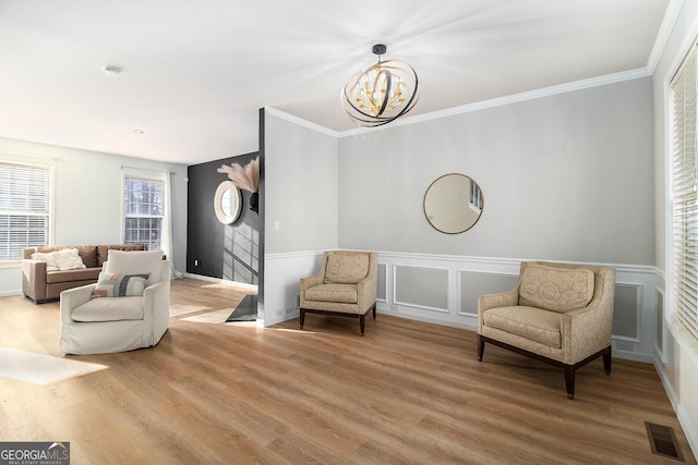 living area featuring wood-type flooring, ornamental molding, and an inviting chandelier