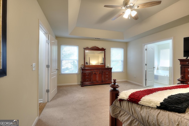 bedroom with a raised ceiling, ceiling fan, light carpet, and ensuite bath