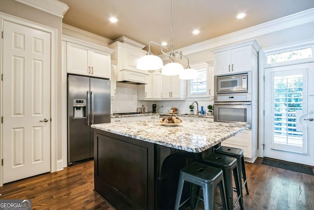 kitchen with pendant lighting, appliances with stainless steel finishes, ornamental molding, white cabinets, and a kitchen island