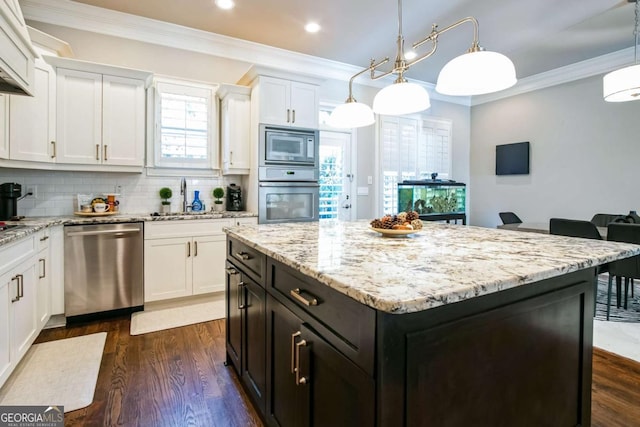 kitchen with sink, appliances with stainless steel finishes, a kitchen island, pendant lighting, and white cabinets