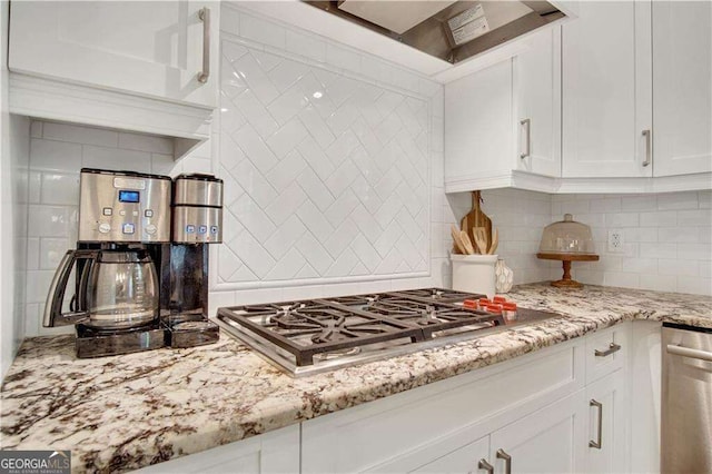 kitchen featuring appliances with stainless steel finishes, backsplash, light stone countertops, white cabinets, and wall chimney exhaust hood