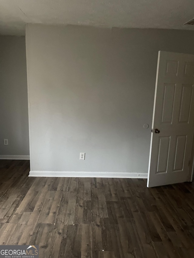 spare room featuring dark wood-style flooring, visible vents, and baseboards