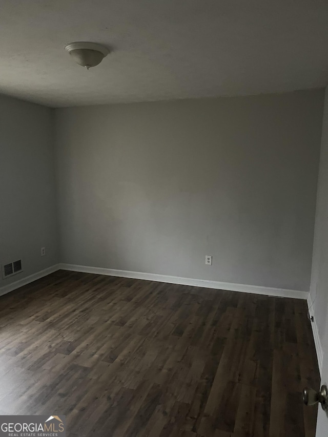 spare room featuring dark wood-style flooring, visible vents, and baseboards