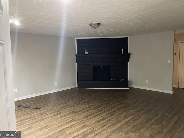 unfurnished living room featuring dark wood-type flooring, a fireplace, a textured ceiling, and baseboards