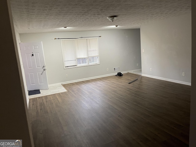 spare room featuring a textured ceiling, dark wood-type flooring, visible vents, and baseboards