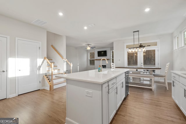 kitchen with sink, light hardwood / wood-style flooring, white cabinetry, hanging light fixtures, and an island with sink