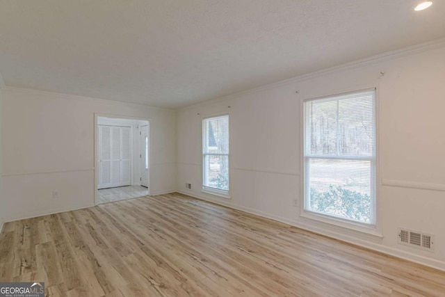 spare room with crown molding, a textured ceiling, and light wood-type flooring