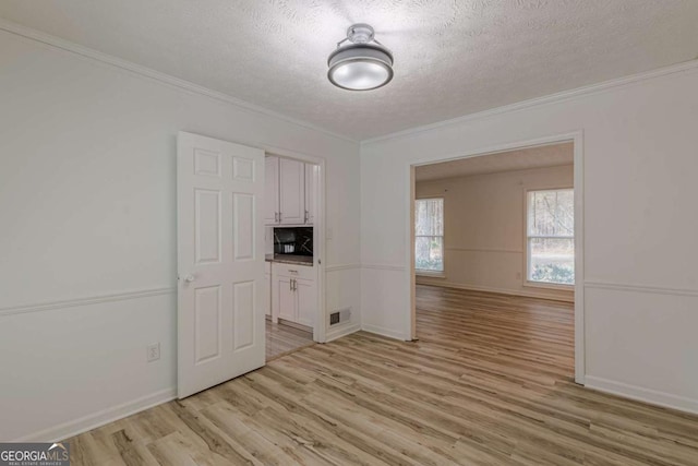 unfurnished room with crown molding, a textured ceiling, and light hardwood / wood-style flooring