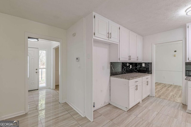 kitchen featuring light stone counters, decorative backsplash, a textured ceiling, and white cabinets