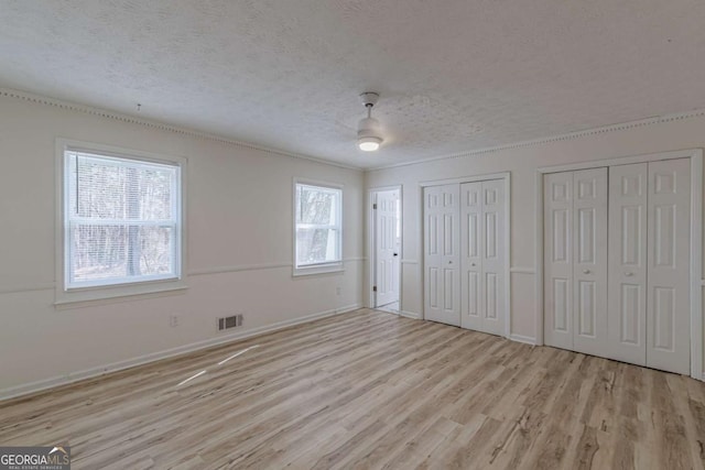 unfurnished bedroom with ceiling fan, two closets, a textured ceiling, and light hardwood / wood-style floors