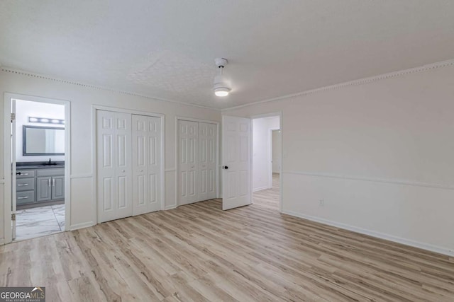 unfurnished bedroom featuring sink, ceiling fan, ensuite bathroom, two closets, and light wood-type flooring