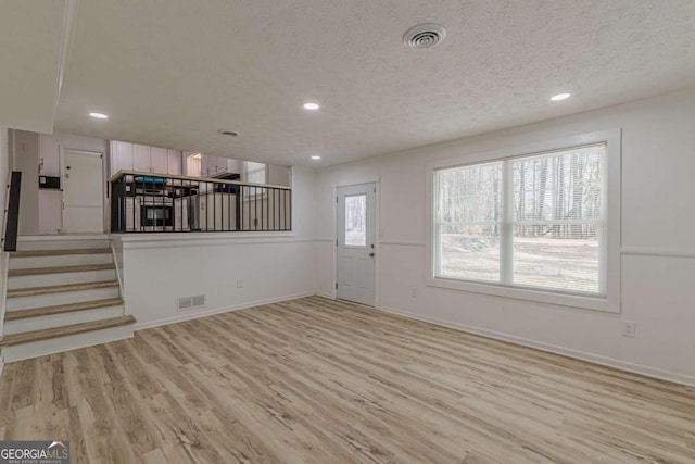 unfurnished living room with light hardwood / wood-style floors and a textured ceiling