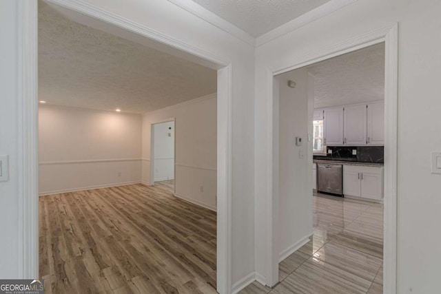 hallway with ornamental molding, a textured ceiling, and light wood-type flooring