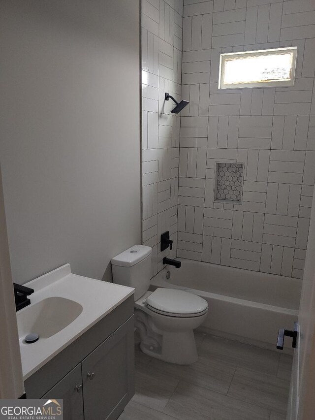 full bathroom featuring tiled shower / bath, vanity, and toilet