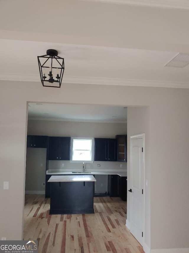 kitchen featuring sink, hanging light fixtures, a center island, ornamental molding, and light wood-type flooring