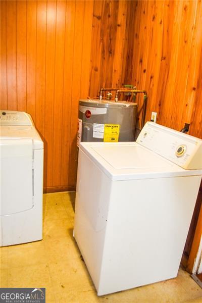 washroom with wooden walls, electric water heater, and washing machine and dryer