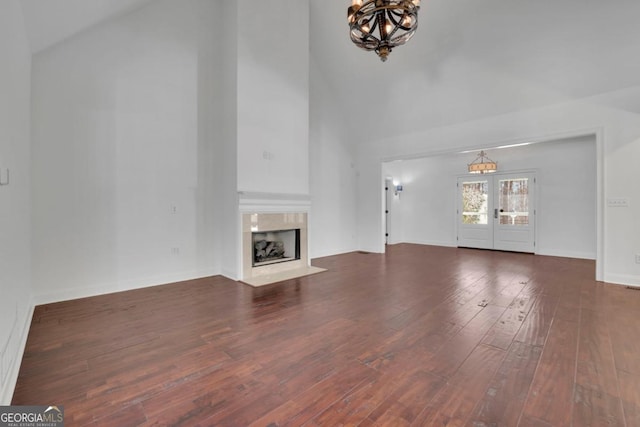 unfurnished living room with high vaulted ceiling, a chandelier, a high end fireplace, dark wood-type flooring, and french doors