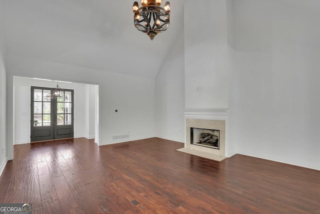 unfurnished living room with french doors, an inviting chandelier, high vaulted ceiling, dark hardwood / wood-style floors, and a premium fireplace