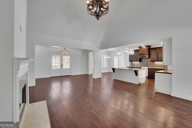 living room featuring an inviting chandelier, dark wood-type flooring, high vaulted ceiling, and french doors