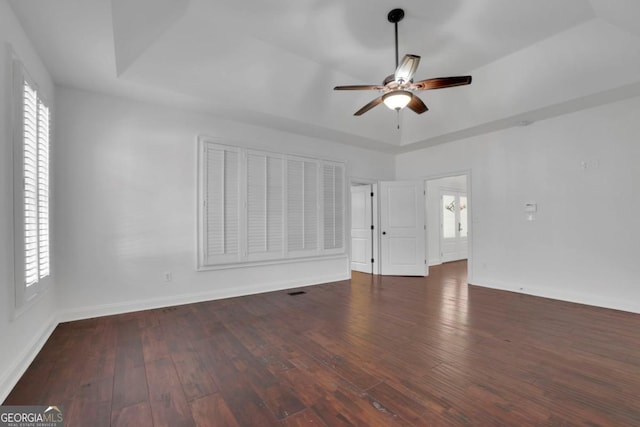 spare room with a raised ceiling, a healthy amount of sunlight, and dark hardwood / wood-style flooring