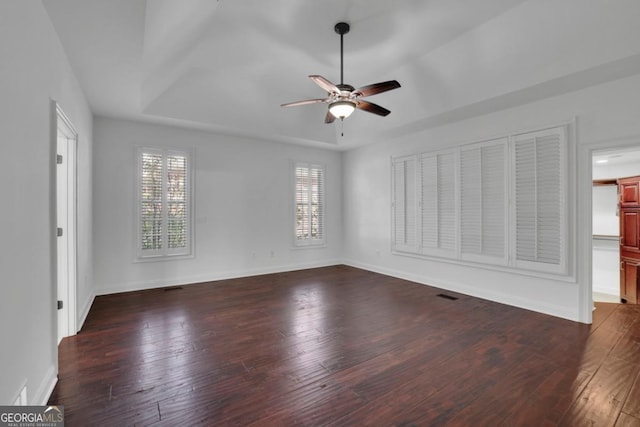 empty room with a tray ceiling, dark hardwood / wood-style floors, and ceiling fan