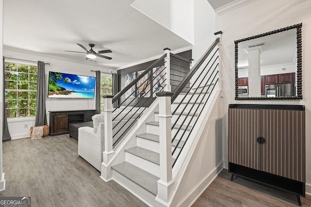 stairs with ceiling fan, ornamental molding, a fireplace, and hardwood / wood-style floors