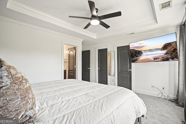 carpeted bedroom featuring a tray ceiling, ornamental molding, ceiling fan, and ensuite bathroom