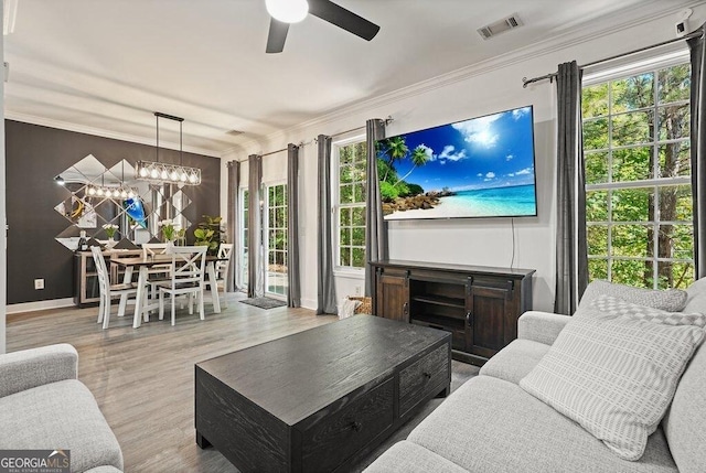 living room featuring ornamental molding, ceiling fan with notable chandelier, and light wood-type flooring