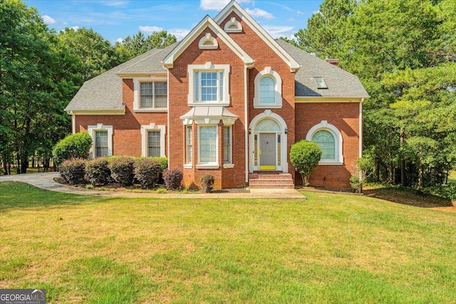 view of front of property with a front lawn, roof with shingles, and brick siding