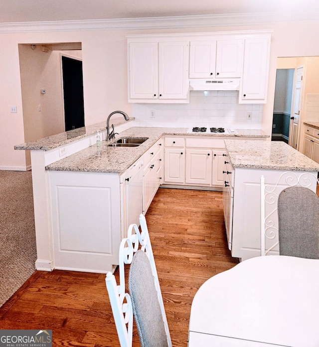 kitchen featuring under cabinet range hood, white cabinetry, a sink, and a peninsula