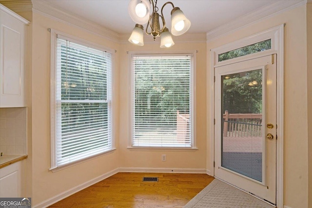 doorway with crown molding, light hardwood / wood-style flooring, and a chandelier