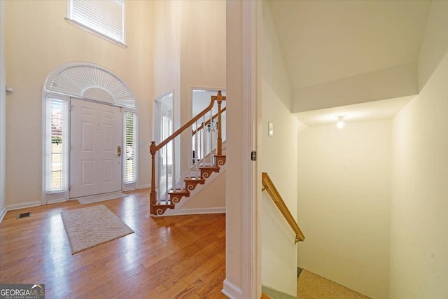 entrance foyer with a high ceiling, visible vents, baseboards, stairway, and light wood finished floors