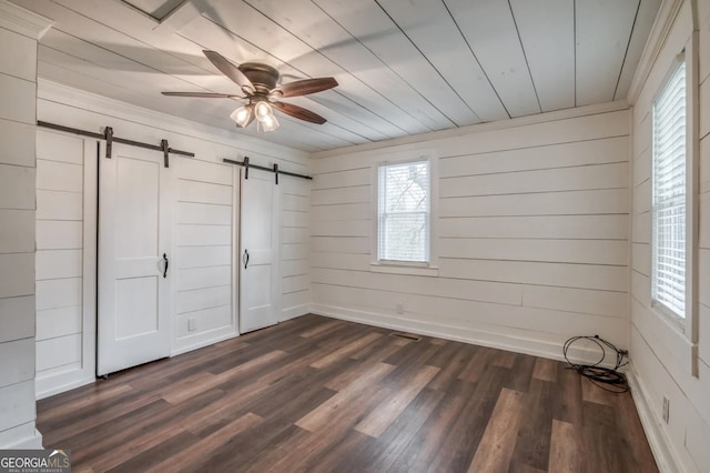 unfurnished bedroom featuring ceiling fan, a barn door, and dark hardwood / wood-style flooring