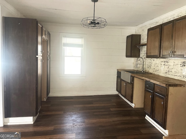 kitchen featuring sink, crown molding, hanging light fixtures, dark brown cabinets, and dark hardwood / wood-style flooring