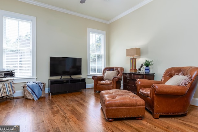 living area featuring plenty of natural light, baseboards, ornamental molding, and wood finished floors