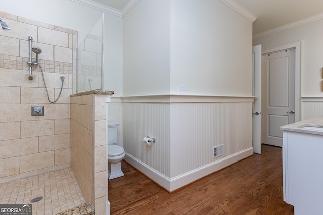 bathroom featuring hardwood / wood-style flooring, vanity, tiled shower, toilet, and crown molding